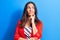 Young beautiful brunette businesswoman wearing jacket standing over blue background thinking concentrated about doubt with finger