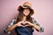 Young beautiful brunette farmer woman wearing apron and hat over pink background smiling in love showing heart symbol and shape