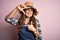 Young beautiful brunette farmer woman wearing apron and hat over pink background smiling making frame with hands and fingers with