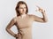 Young beautiful brunette girl frowns and shows small size measure with her hand gesture on a white isolated background