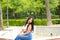 Young and beautiful brunette and latin woman, sitting cross-legged on the edge of a park fountain and resting. The woman is happy