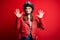 Young beautiful brunette motocyclist woman wearing motorcycle helmet and red jacket showing and pointing up with fingers number