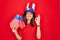 Young beautiful brunette patriotic woman wearing united states hat holding usa flags doing ok sign with fingers, smiling friendly