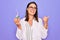 Young beautiful brunette scientist woman wearing coat and glasses holding test tube pointing thumb up to the side smiling happy