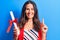 Young beautiful brunette smart woman holding graduated degree diploma over blue background smiling with an idea or question