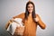 Young beautiful brunette woman doing housework chores holding wicker basket with clothes happy with big smile doing ok sign, thumb