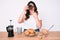 Young beautiful brunette woman eating breakfast holding cholate donut covering mouth with hand, shocked and afraid for mistake