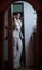 Young beautiful brunette woman in elegant white suit with trousers standing in door frame. Seductive dark hair girl posing indoors