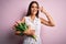 Young beautiful brunette woman holding bouquet of tulips flowers over pink background Doing peace symbol with fingers over face,