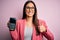 Young beautiful brunette woman holding dataphone paying with credit card to finance happy with big smile doing ok sign, thumb up