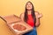 Young beautiful brunette woman holding delivery box with italian pizza screaming proud, celebrating victory and success very