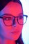 Young beautiful brunette woman with pink neon backlit face wearing eyeglasses