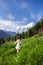 Young beautiful brunette woman walking through wildflowers in alpine meadow, summer dress, mountain, sunlight