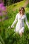 Young beautiful brunette woman walking through wildflowers in alpine meadow, summer dress, mountain, sunlight