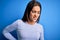 Young beautiful brunette woman wearing casual sweater standing over blue background Suffering of backache, touching back with