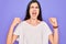 Young beautiful brunette woman wearing casual white t-shirt over purple background angry and mad raising fists frustrated and