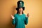 Young beautiful brunette woman wearing green hat with clover celebrating saint patricks day crazy and mad shouting and yelling