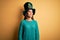 Young beautiful brunette woman wearing green hat with clover celebrating saint patricks day looking away to side with smile on