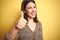 Young beautiful brunette woman wearing leopard shirt over yellow isolated background doing happy thumbs up gesture with hand