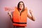 Young beautiful brunette woman wearing lifejacket holding paper with danger message annoyed and frustrated shouting with anger,