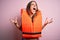 Young beautiful brunette woman wearing orange lifejacket over isolated pink background crazy and mad shouting and yelling with