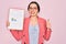 Young beautiful business woman with blue eyes wearing glasses holding clipboard happy with big smile doing ok sign, thumb up with