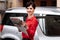 Young beautiful business woman with red lipstick in glasses and red polka dots blouse standing by her luxurious car