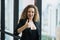 Young beautiful business woman standing near window in office. Smiling sexy lady confident in black suited showing thumbs up