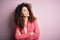 Young beautiful businesswoman with curly hair and piercing wearing elegant jacket looking to the side with arms crossed convinced