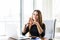 Young beautiful businesswoman working on laptop and keeping hand on chin while sitting at her working place