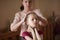 Young beautiful caring woman fixing her ballerina dancer little thin daughter hair before concert show
