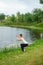 Young beautiful caucasian brunette girl doing yoga on a green lawn against the background of the river. Eagle Pose, Garudasana