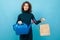 Young and beautiful caucasian girl with curly hair keeps green watering can and eco-friendly paper bag and smiles