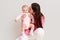 Young beautiful Caucasian mother with long dark hair posing with newborn infant baby dresses bodysuit and socks. Female wearing