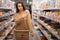 Young beautiful caucasian woman with a disgruntled look in the supermarket, the index finger of the hand is directed to the shelf