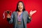 Young beautiful champion asian woman holding trophy wearing medals over red background very happy and excited, winner expression