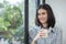 Young beautiful cheerful woman holding paper cup coffee smiling looking out window office. asian business woman relax time