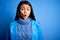 Young beautiful chinese woman wearing rain coat standing over isolated blue background afraid and shocked with surprise