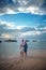 Young beautiful couple in Santa Claus hats walks along the shore of the tropical sea at sunset in the resort, vacation and travel