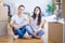 Young beautiful couple sitting on the floor at new home around cardboard boxes with serious expression on face