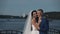 Young beautiful couple standing on the quay of river and hugging in their wedding day. Newlyweds spending time together.