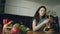 Young beautiful curly pretty caucasian woman sitting at table in nice kitchen using smartphone, she is texting someone