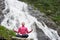 Young beautiful female practising yoga on stone in front of beautiful Balea waterfall in Romania