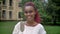 Young beautiful female student with pink dreadlocks smiling at camera and standing in park near university, happy anf