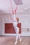 Young beautiful flexible girl in white jumpsuit is posing in a dance studio. Stretching and body ballet theme. Modern dance trend