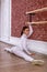 Young beautiful flexible girl in white jumpsuit is posing in a dance studio. Stretching and body ballet theme. Modern dance trend