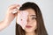 Young beautiful funny woman holding slice of ham near her eye looking hungry isolated white background