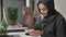 Young beautiful girl in black hijab sits in office and uses smartphone. Girl in black hijab in the background. Arab