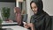 Young beautiful girl in black hijab sits in office and uses smartphone. Girl in black hijab in the background. Arab