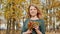 Young beautiful girl in dress with bouquet of autumn leaves posing in camera enjoying autumn in city park.